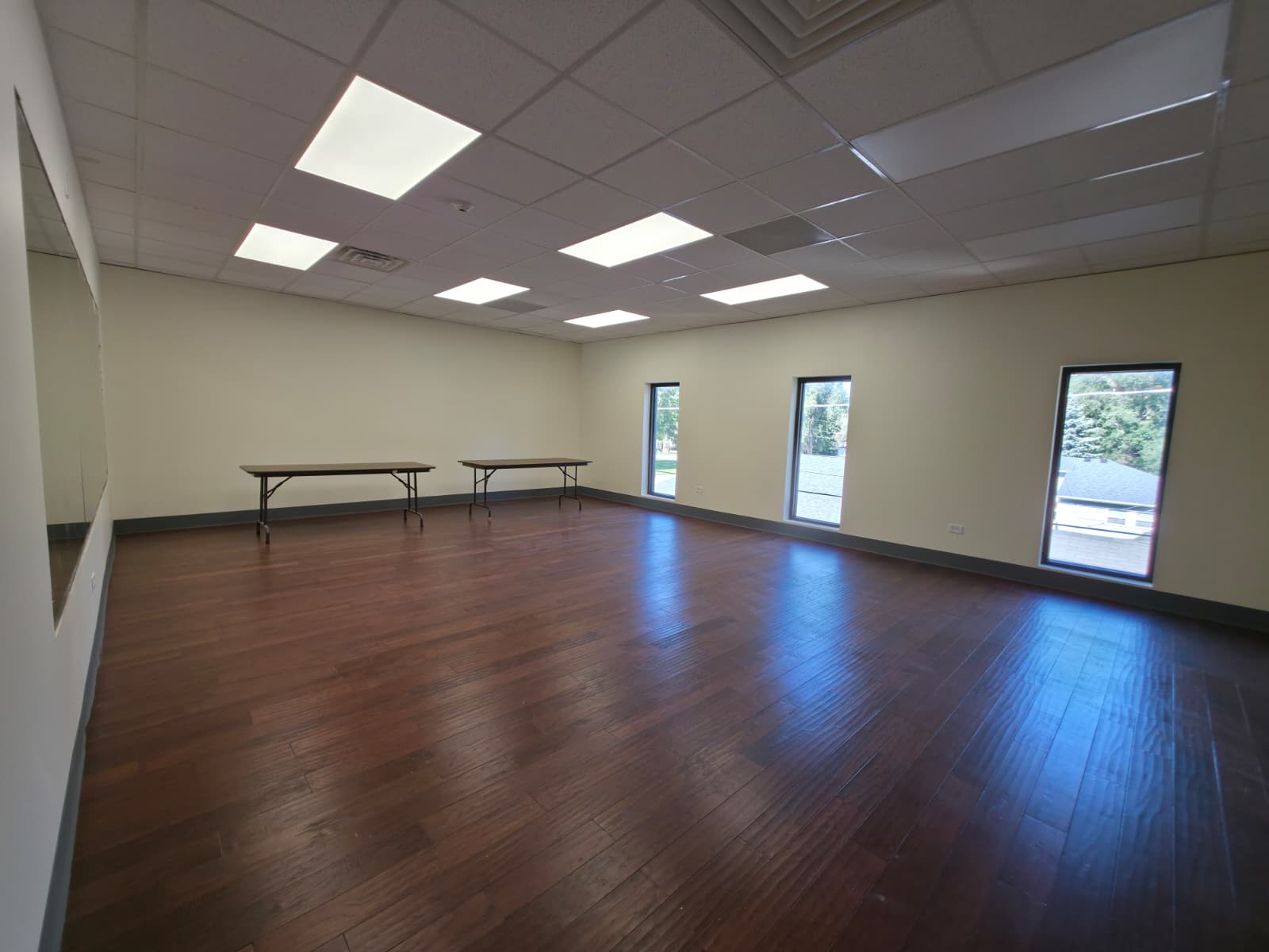 The Studio Room with wood flooring, a wall mirror, tall windows and rectangular tables at the back